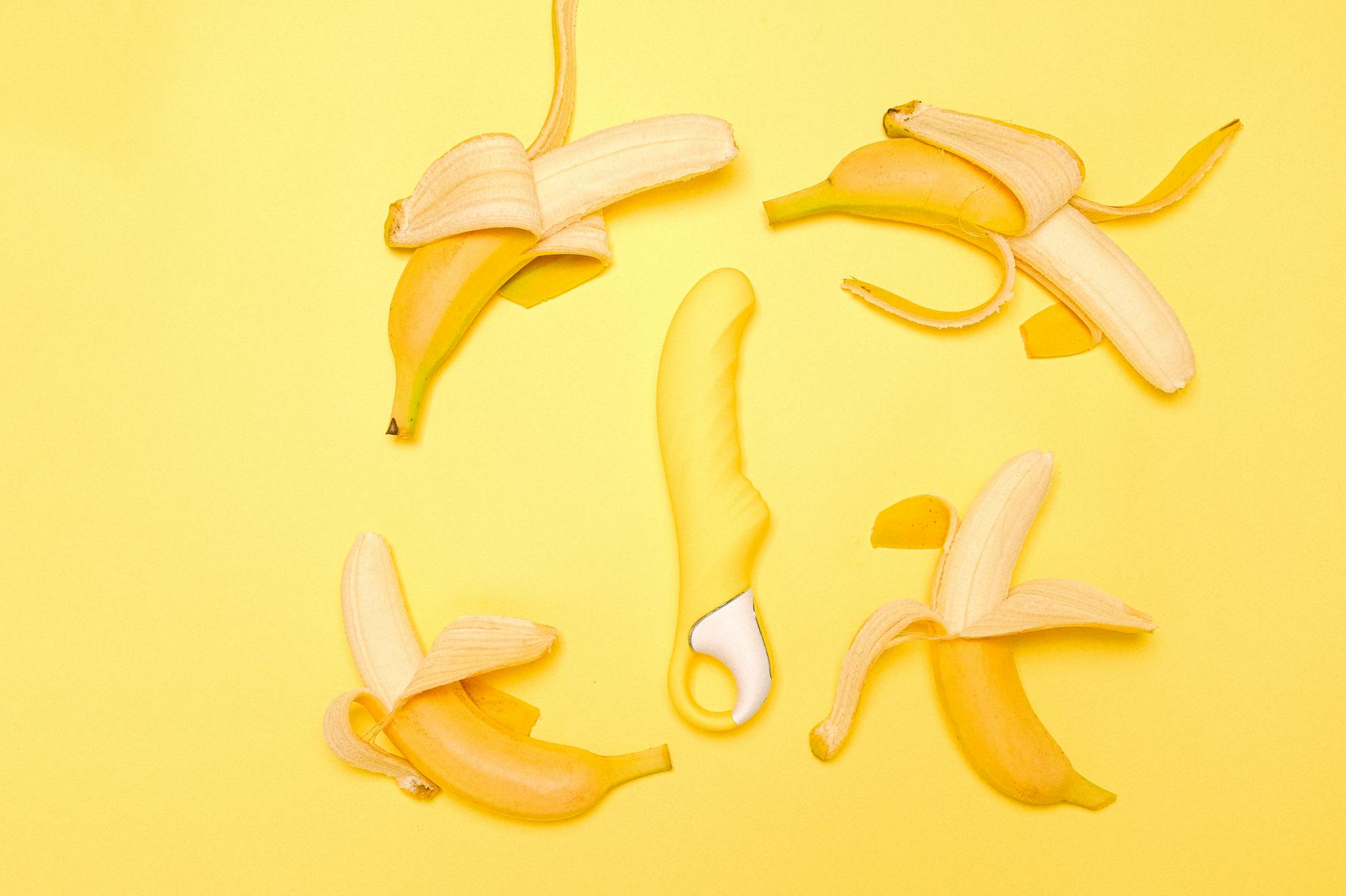 Yellow lemon clitoral vibrator on a bright yellow background surrounded by peeled bananas
