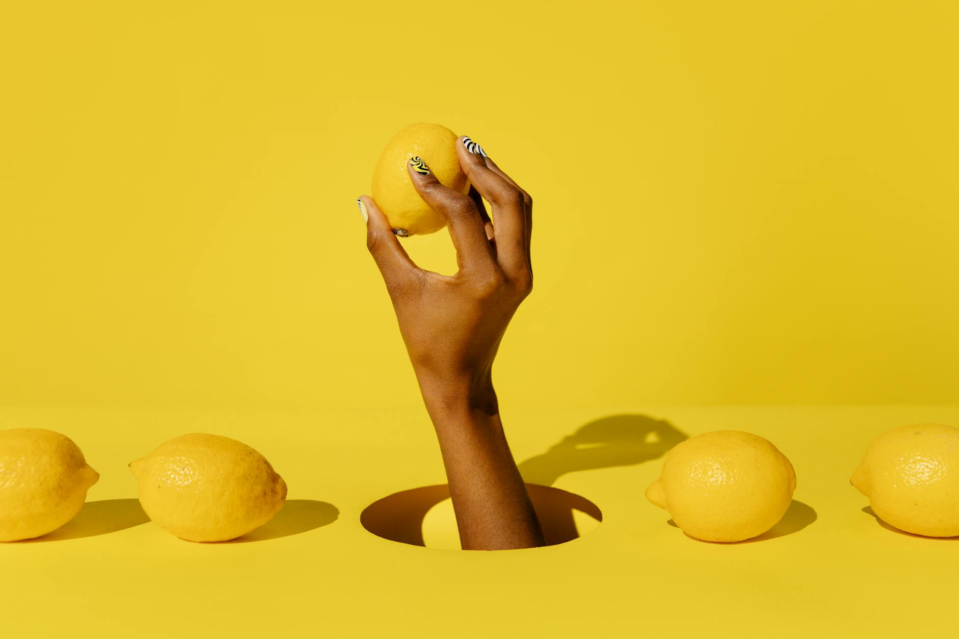 A hand holding a fresh lemon against a bright yellow background, symbolizing rediscovery and renewal