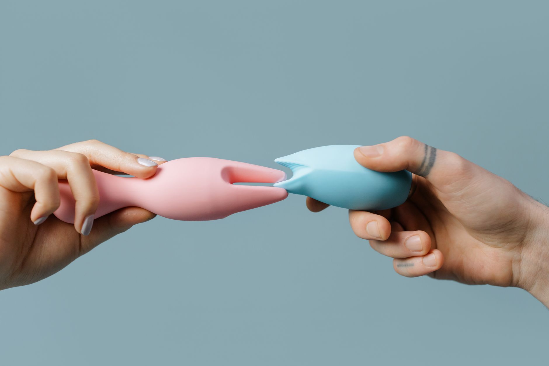 Hand holding a blue clitoral vibrator against a purple background