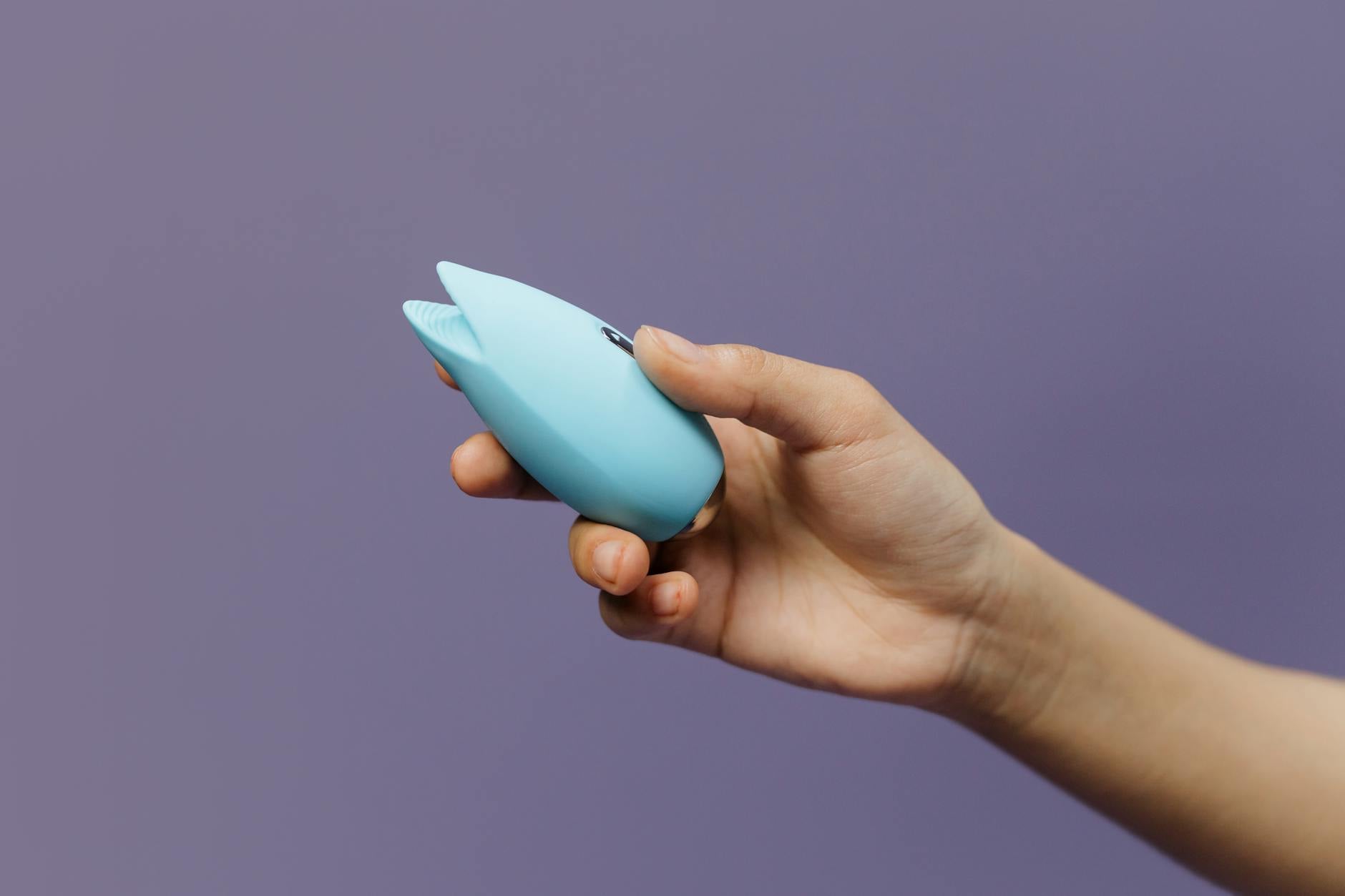 Close-up of hands holding a blue personal massager against a knitted sweater