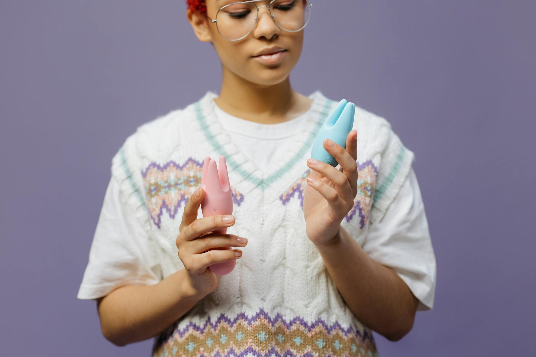 Woman holding blue and pink clitoral vibrators in contemplative pose, representing mindful pleasure exploration.